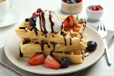 Delicious Belgian waffles with ice cream, berries and chocolate sauce served on white wooden table, closeup