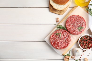 Photo of Raw hamburger patties with rosemary and pepper on white wooden table, flat lay. Space for text