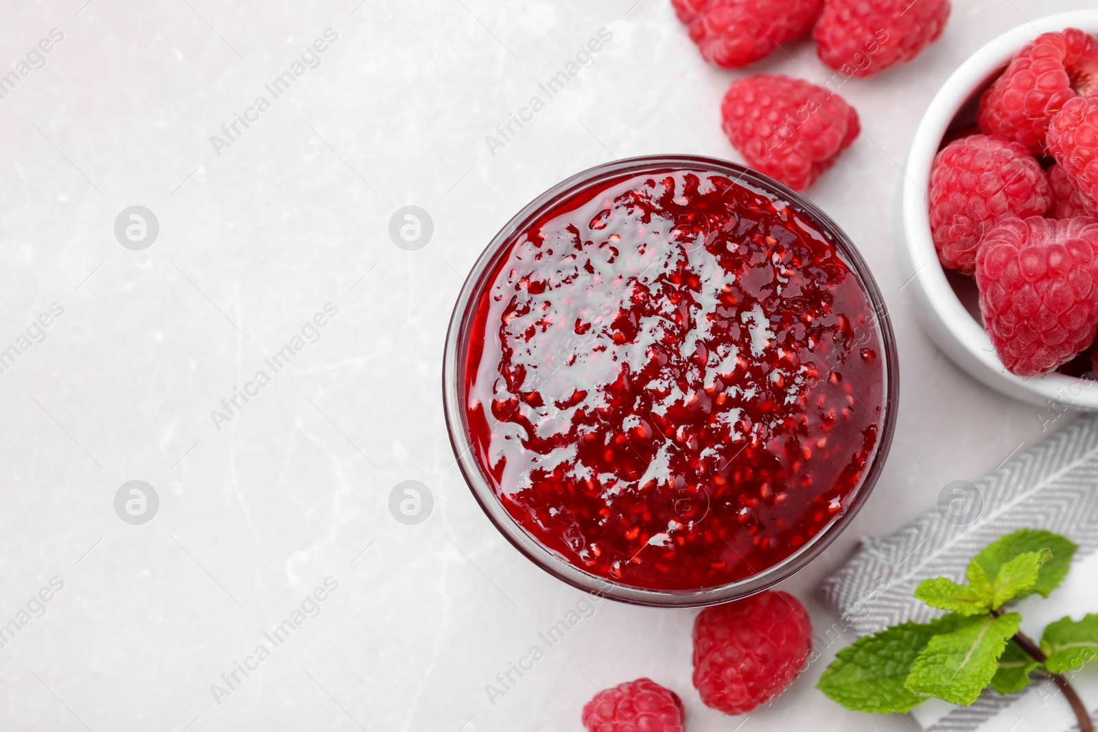 Photo of Delicious jam and fresh raspberries on white table, flat lay. Space for text