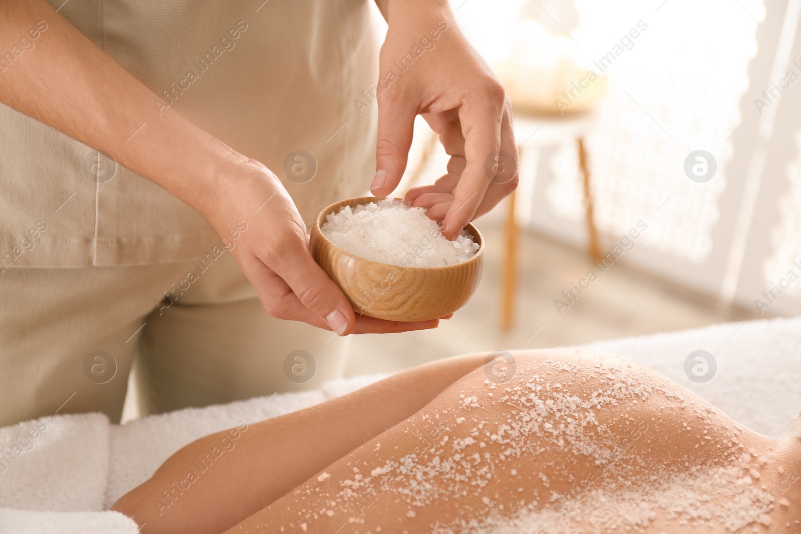 Photo of Young woman having body scrubbing procedure with sea salt in spa salon, closeup