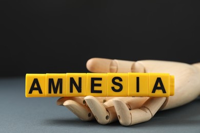 Photo of Amnesia. Mannequin hand with yellow cubes on grey background, closeup