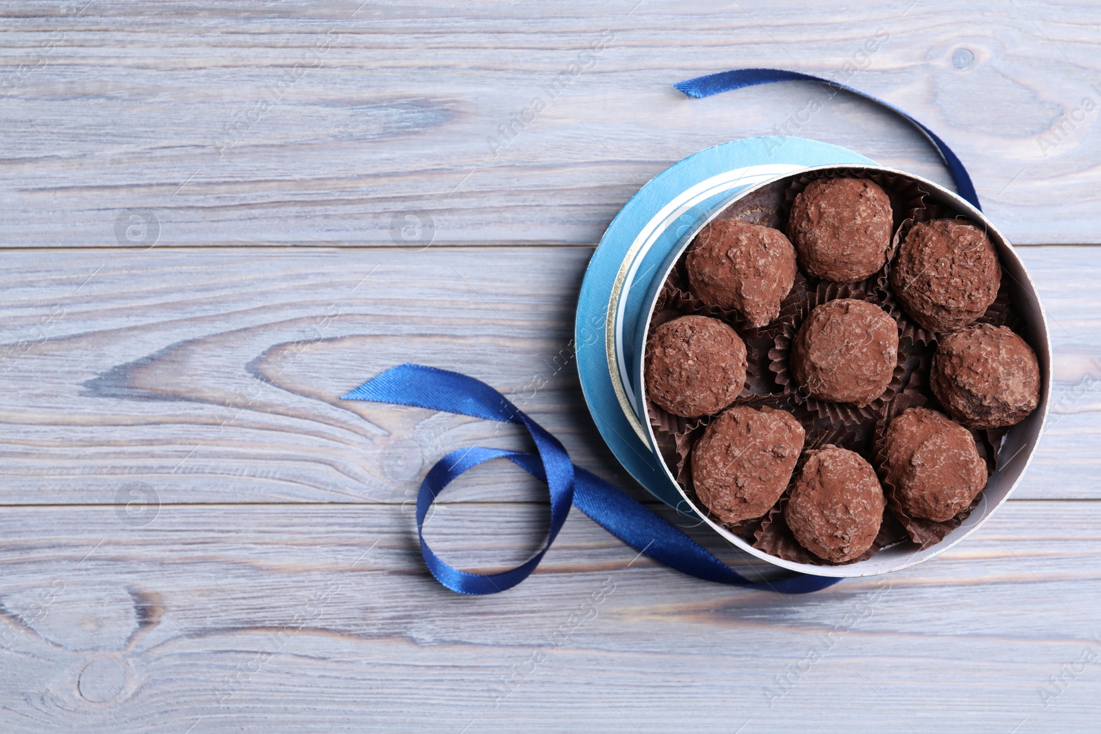 Photo of Box with tasty chocolate truffle candies on wooden table, flat lay. Space for text