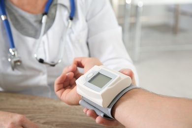 Doctor checking man's pulse with medical device in hospital, closeup