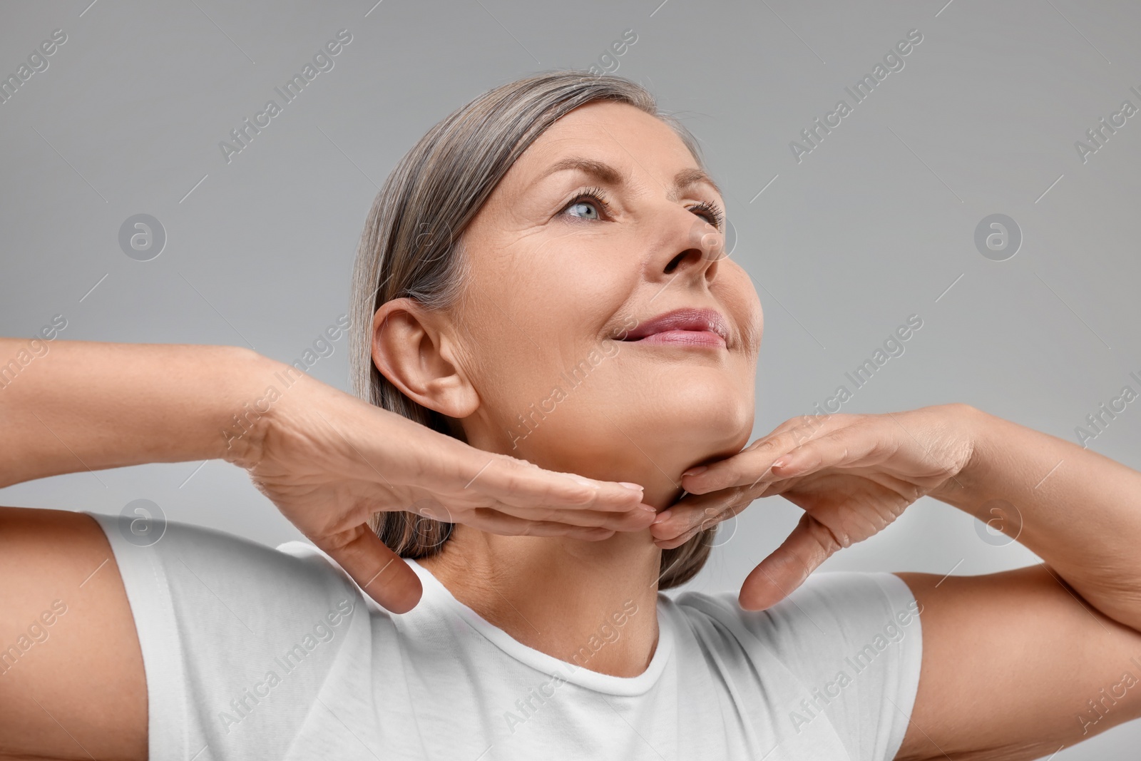 Photo of Beautiful woman touching her neck on grey background, low angle view