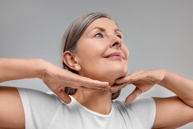 Beautiful woman touching her neck on grey background, low angle view