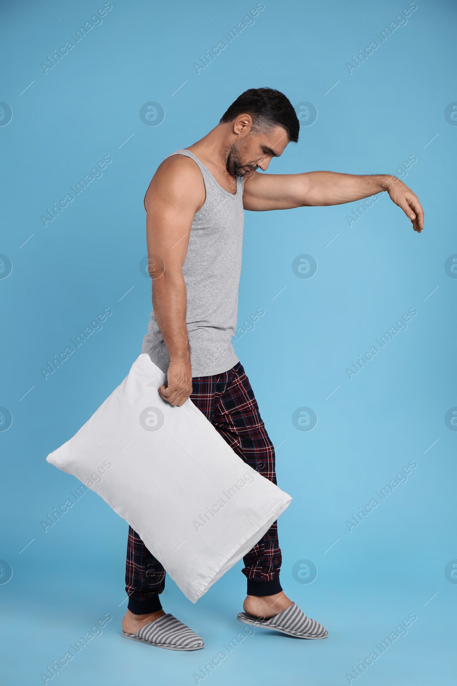 Photo of Man with pillow in sleepwalking state on light blue background