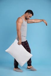 Photo of Man with pillow in sleepwalking state on light blue background