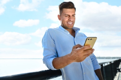 Photo of Handsome man using modern mobile phone near river, focus on hand