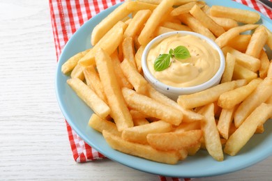 Photo of Delicious French fries and cheese sauce with basil on white wooden table, closeup