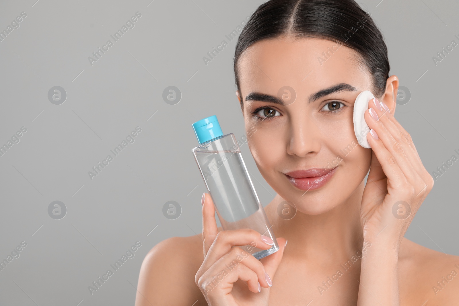 Photo of Beautiful woman removing makeup with cotton pad on light grey background. Space for text