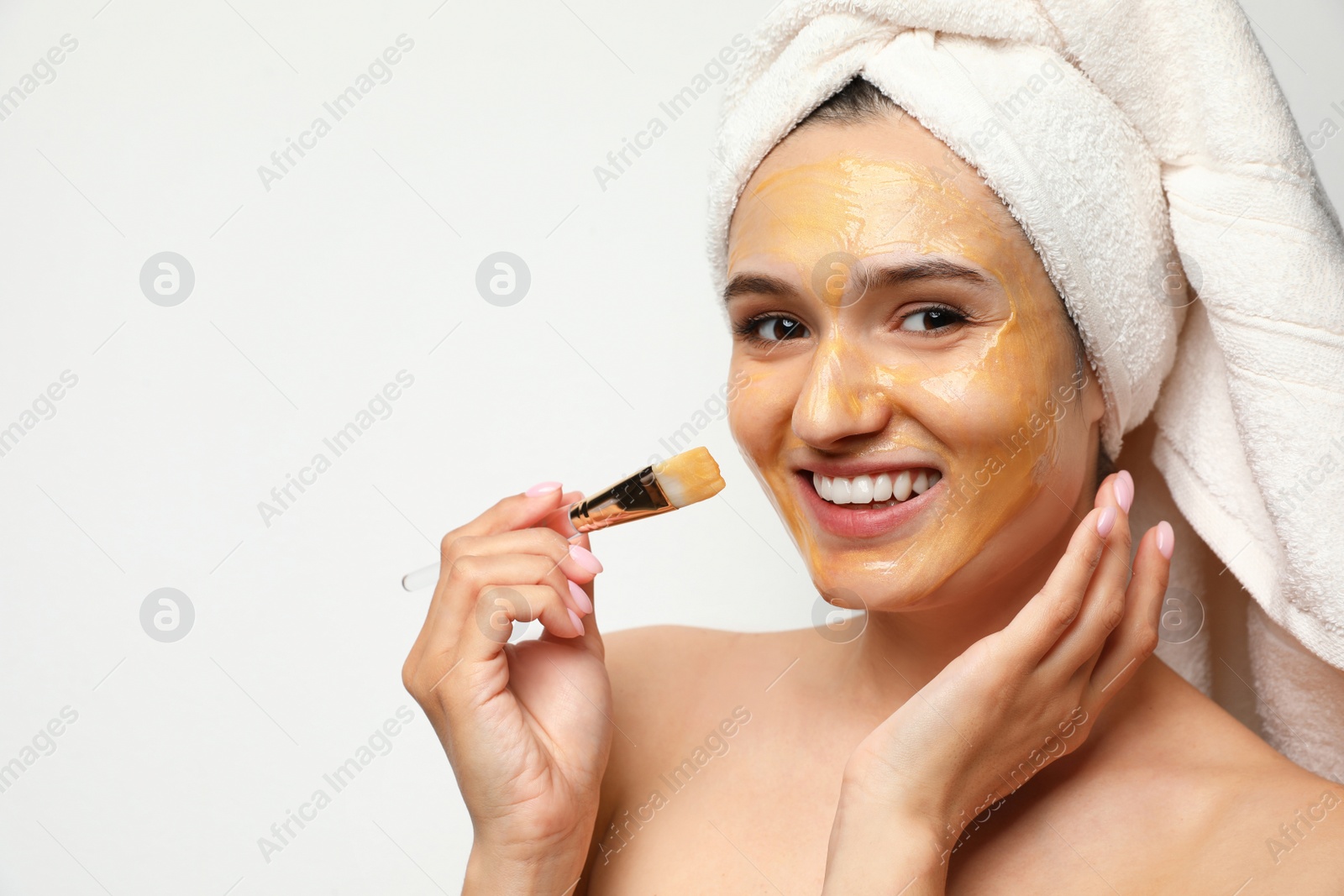 Photo of Beautiful woman applying mask onto face against light background. Space for text