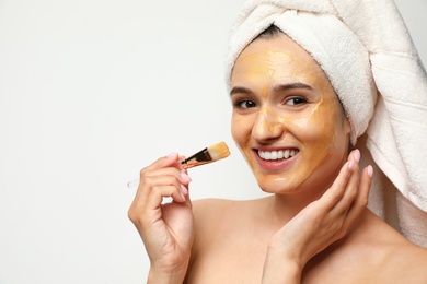 Beautiful woman applying mask onto face against light background. Space for text