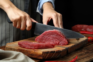 Photo of Woman cutting fresh raw meat at wooden table, closeup