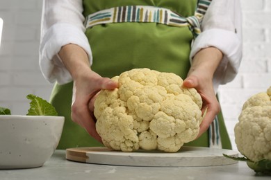 Woman with fresh cauliflower at light grey table, closeup