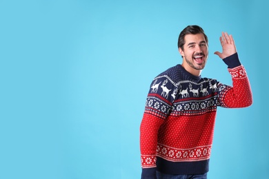 Photo of Portrait of happy young man in Christmas sweater on light blue background. Space for text