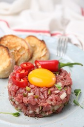 Photo of Tasty beef steak tartare served with yolk and other accompaniments on plate, closeup