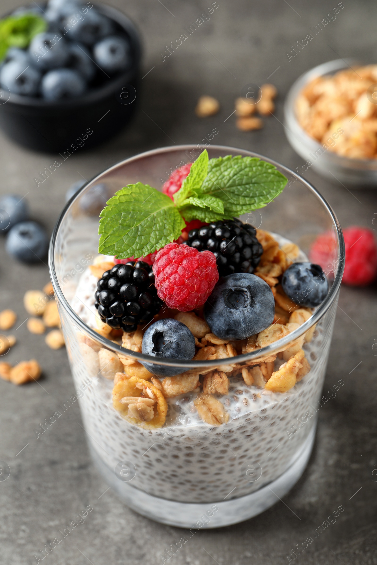 Photo of Delicious chia pudding with berries, granola and mint on grey table, closeup