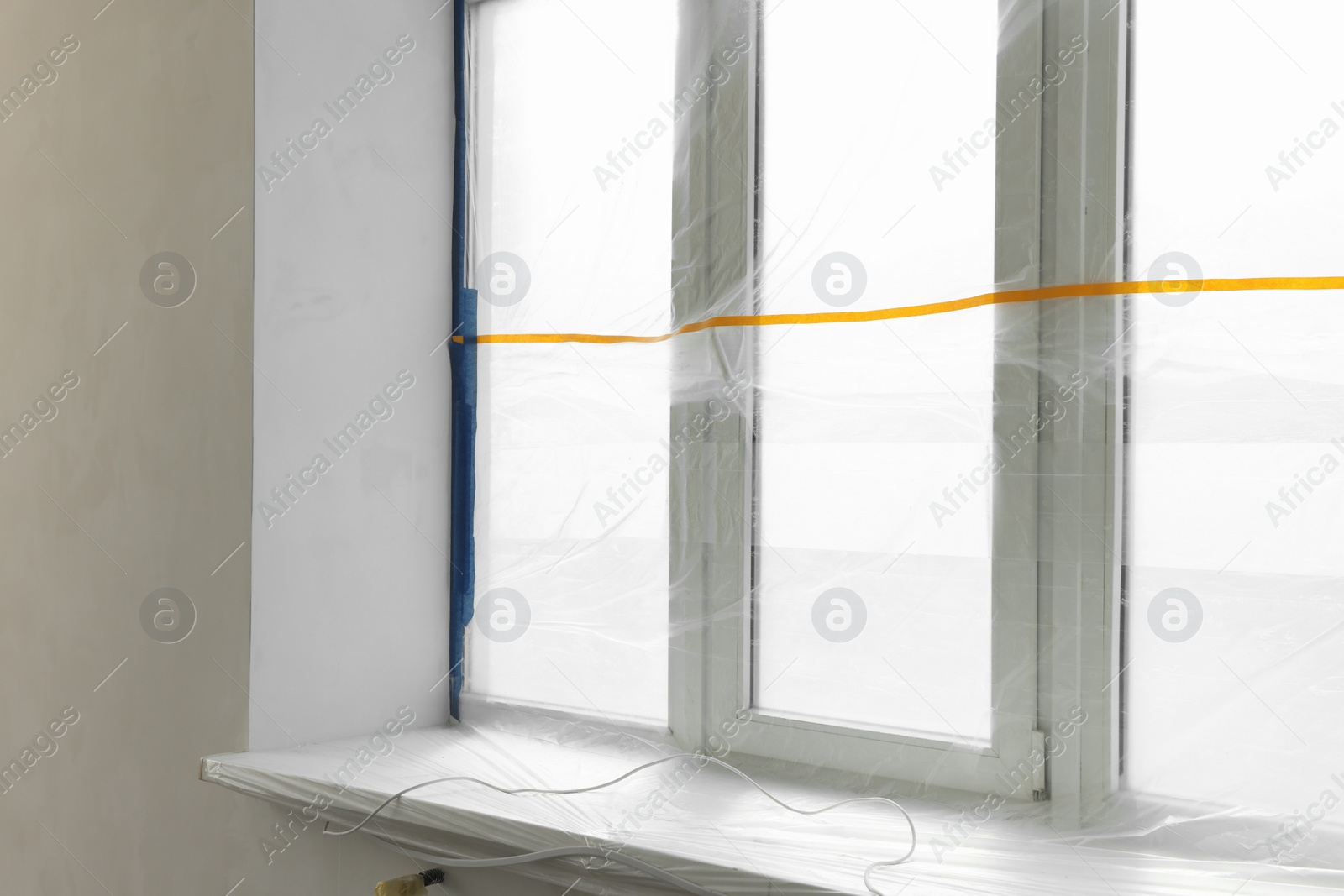 Photo of Window covered by plastic film and insulation tape indoors