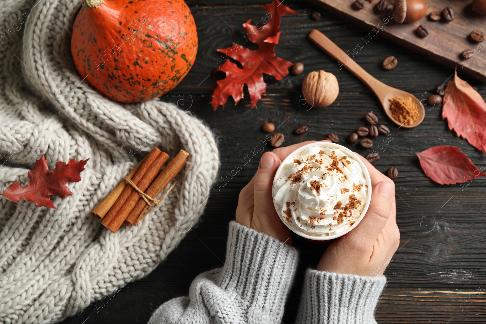 Photo of Woman holding cup with tasty pumpkin spice latte at black wooden table, top view