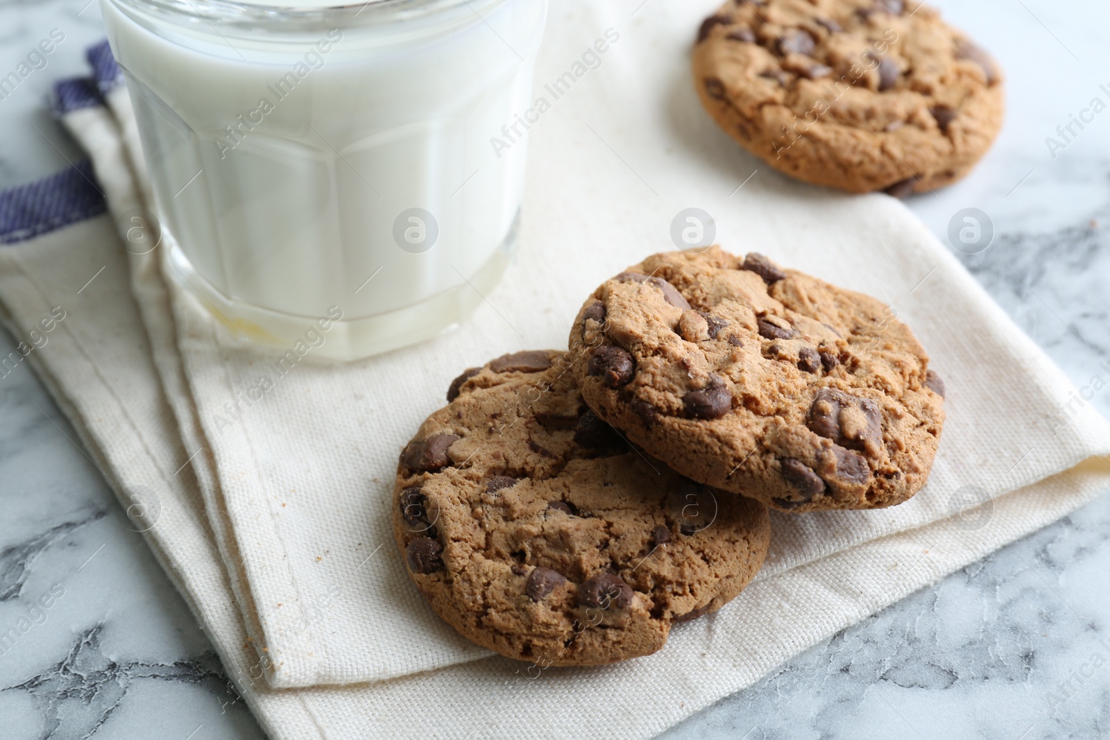 Photo of Tasty chocolate chip cookies and glass of milk on white marble table, closeup