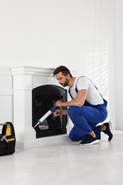 Photo of Professional technician sealing electric fireplace with caulk near white wall in room