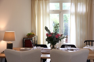 Photo of Stylish dining room with comfortable furniture, big window and bouquet of roses