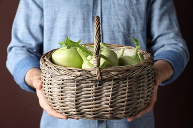 Photo of Man holding wicker basket with ripe kohlrabi plants on brown background, closeup