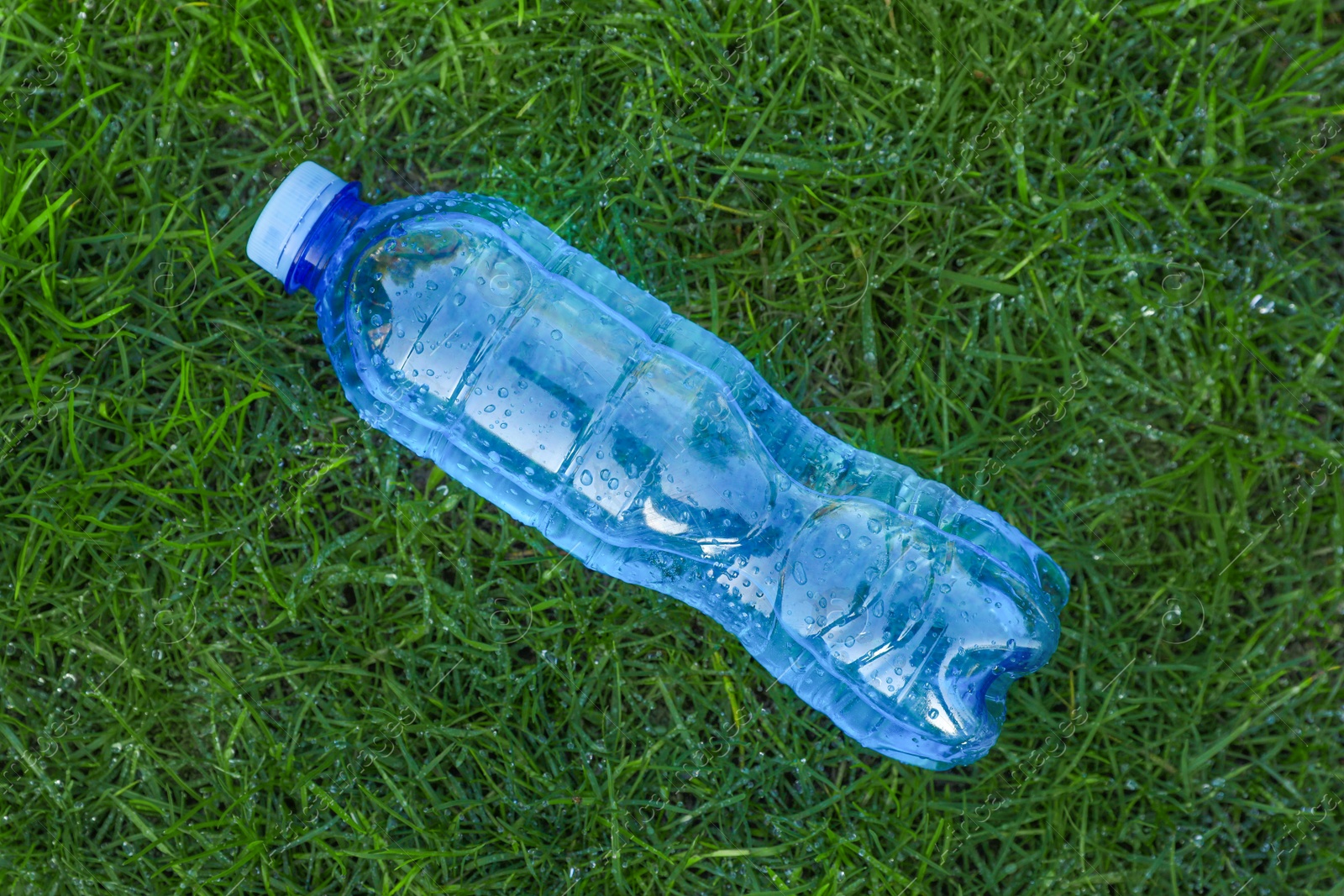 Photo of Plastic bottle of water on green grass outdoors, top view