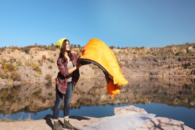 Young female camper with sleeping bag in wilderness. Space for text