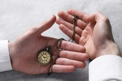 Man holding chain with elegant pocket watch at grey textured table, closeup