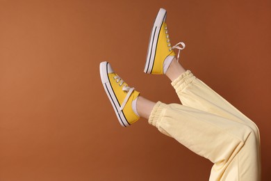 Photo of Woman wearing yellow classic old school sneakers on brown background, closeup
