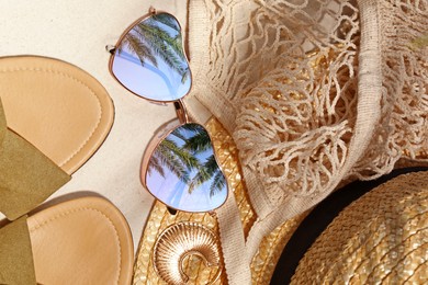 Image of Flat lay composition with stylish sunglasses and other fashionable accessories on sand. Sky and palm trees reflecting in lenses