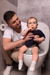 Father training his child to sit on toilet bowl indoors