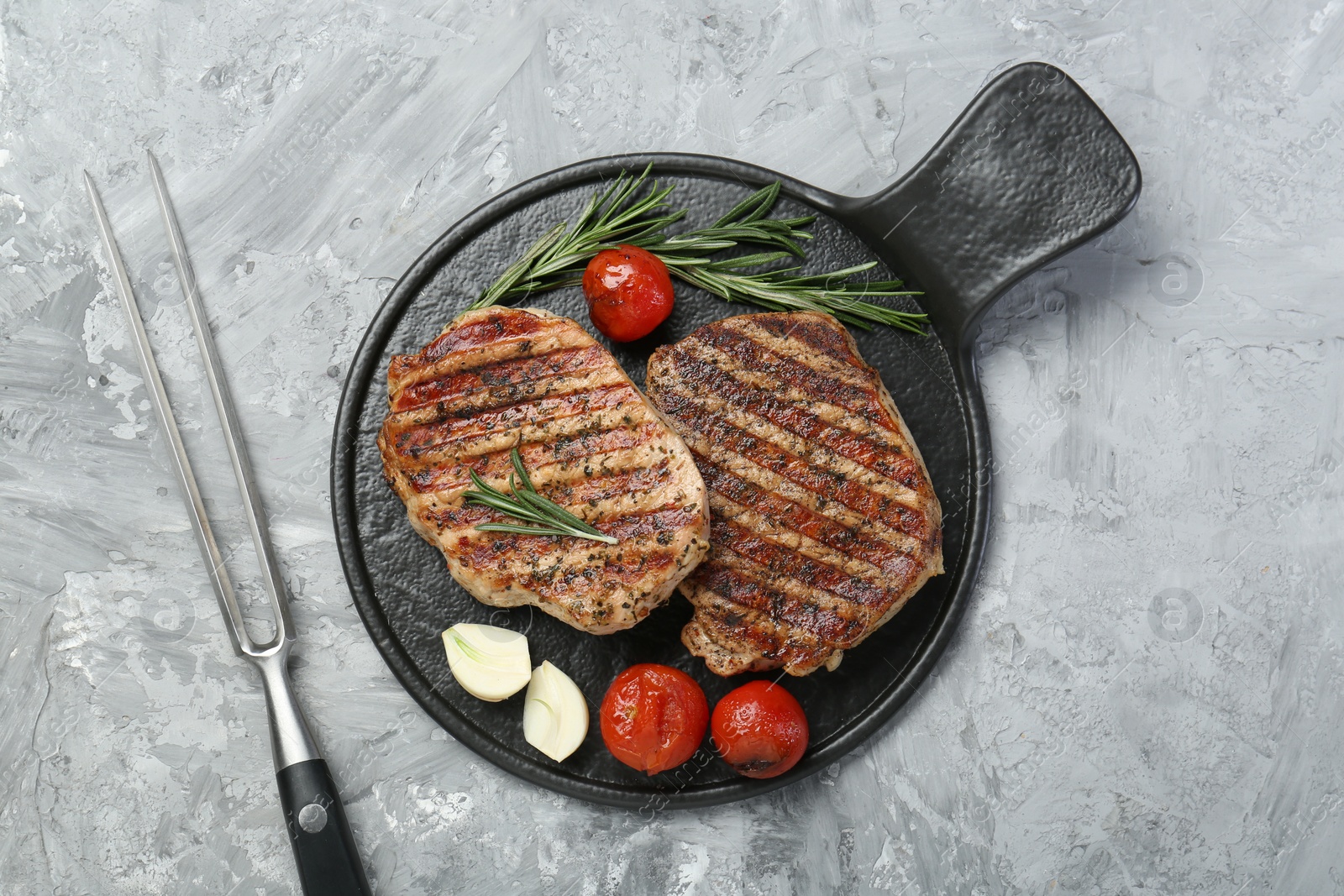 Photo of Delicious grilled pork steaks with spices and meat fork on gray textured table, top view