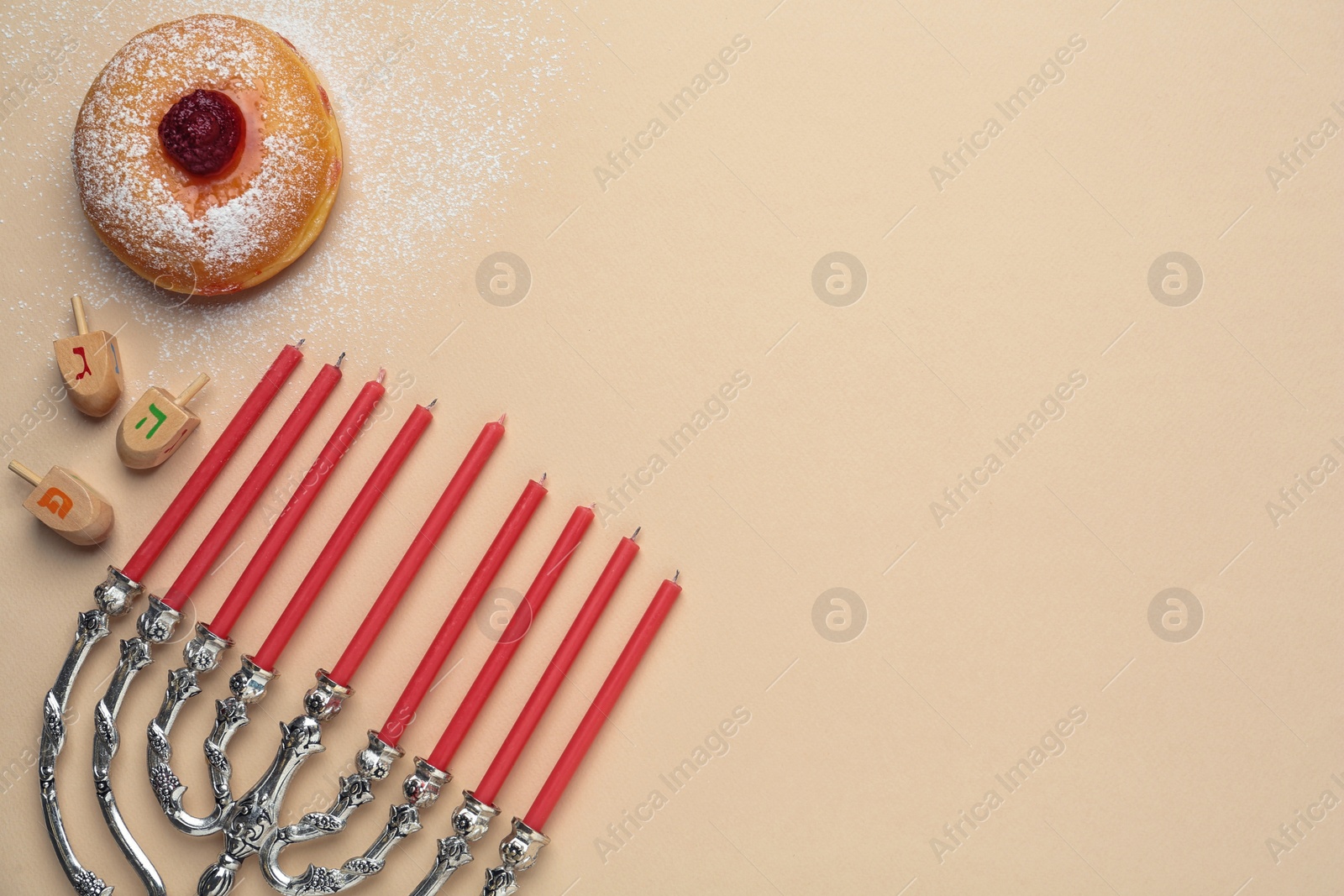 Photo of Hanukkah traditional menorah, candles, doughnut, dreidels with letters He, Pe, Nun, Gimel on beige background, flat lay. Space for text