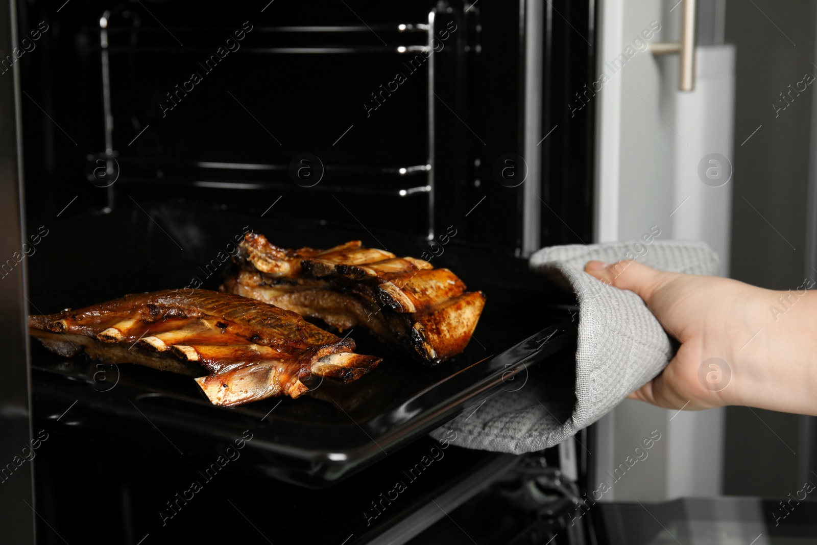 Photo of Woman taking delicious roasted ribs out of oven, closeup