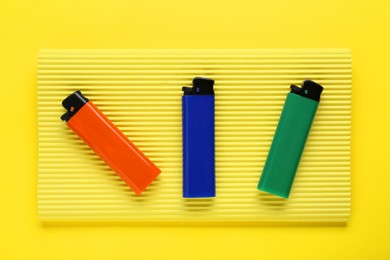 Stylish small pocket lighters with corrugated fiberboard on yellow background, top view