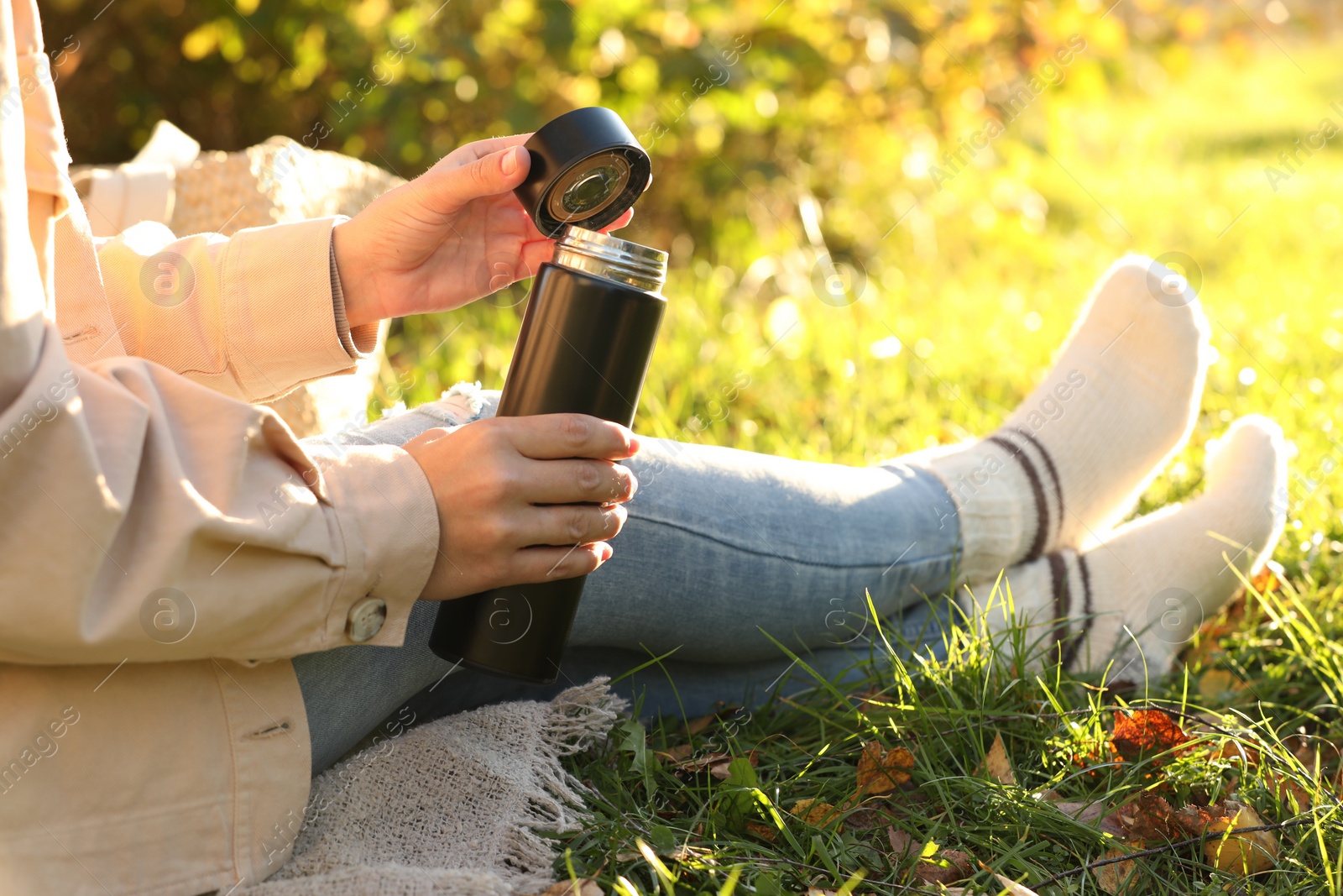 Photo of Woman opening thermos on green grass outdoors, closeup