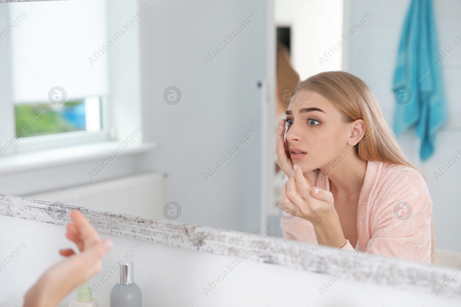 Photo of Young woman with eyelash loss problem looking in mirror indoors