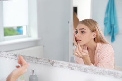 Photo of Young woman with eyelash loss problem looking in mirror indoors