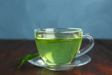 Photo of Cup of aromatic green tea and leaves on wooden table