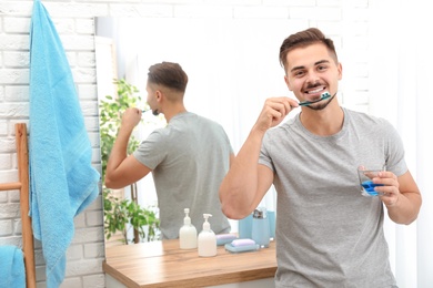 Photo of Young man brushing teeth in bathroom at home. Space for text