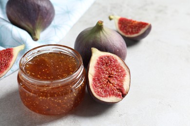 Photo of Jar of tasty sweet jam and fresh figs on light table, closeup. Space for text