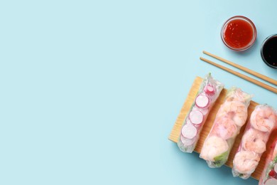 Photo of Different delicious spring rolls, chopsticks and sauces on light blue background, flat lay. Space for text