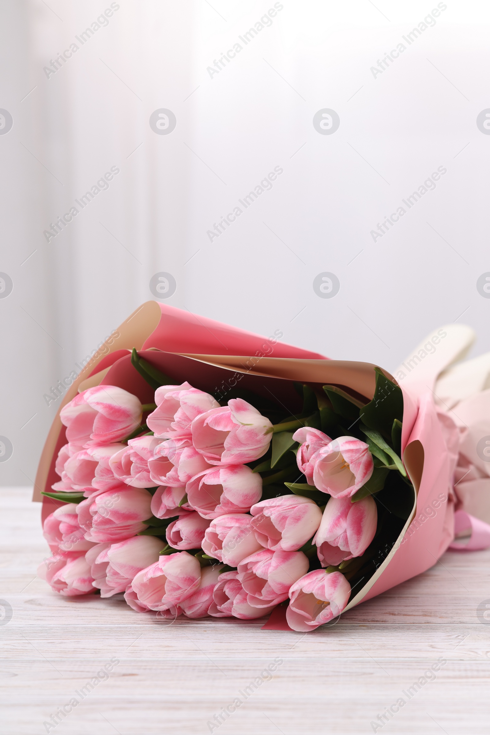 Photo of Beautiful bouquet of fresh pink tulips on white wooden table indoors