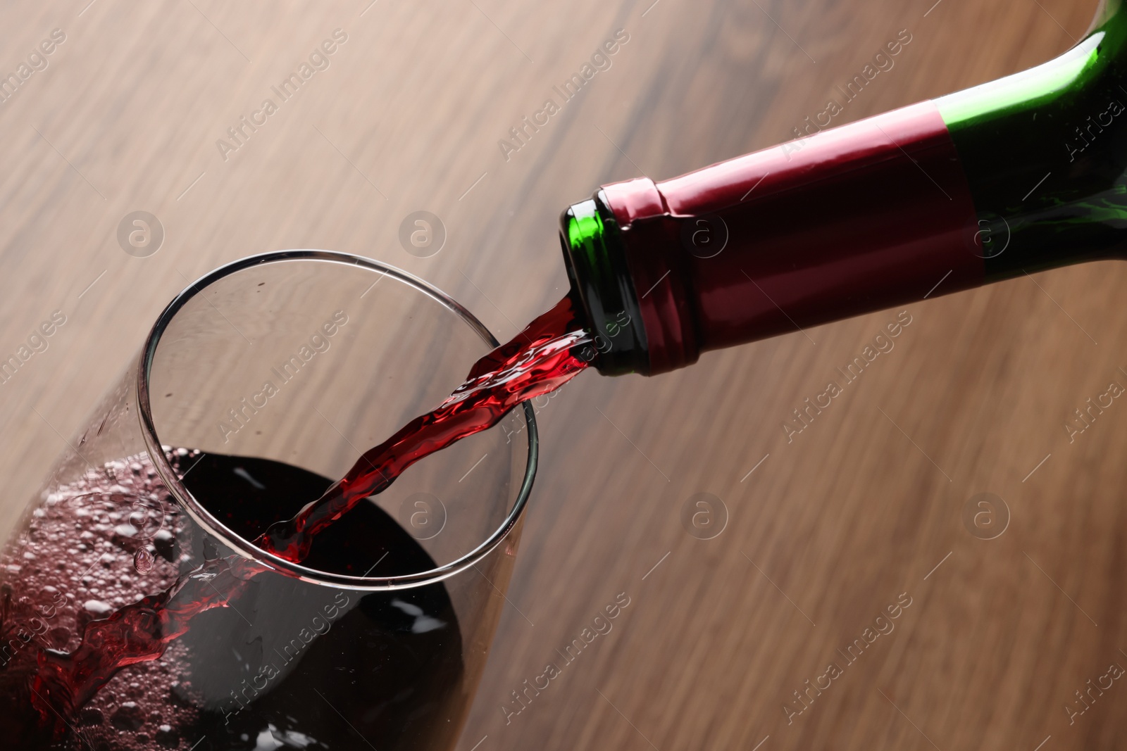 Photo of Pouring tasty red wine in glass at wooden table, closeup