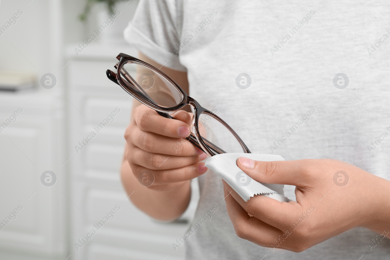 Photo of Woman wiping her glasses with microfiber cloth at home, closeup