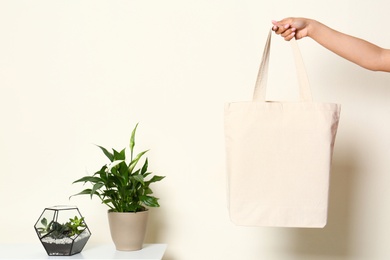 Photo of Woman with stylish blank eco bag near white wall, closeup. Space for text