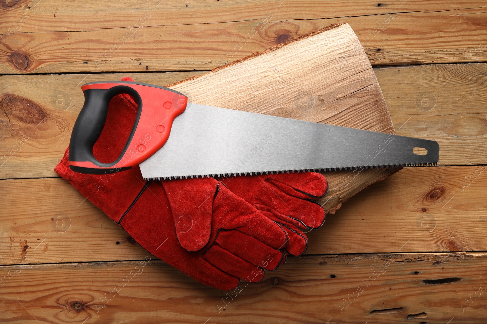 Photo of Saw with colorful handle and gloves on wooden background, top view