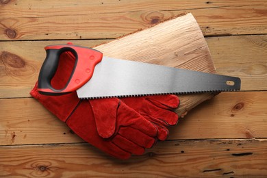 Photo of Saw with colorful handle and gloves on wooden background, top view